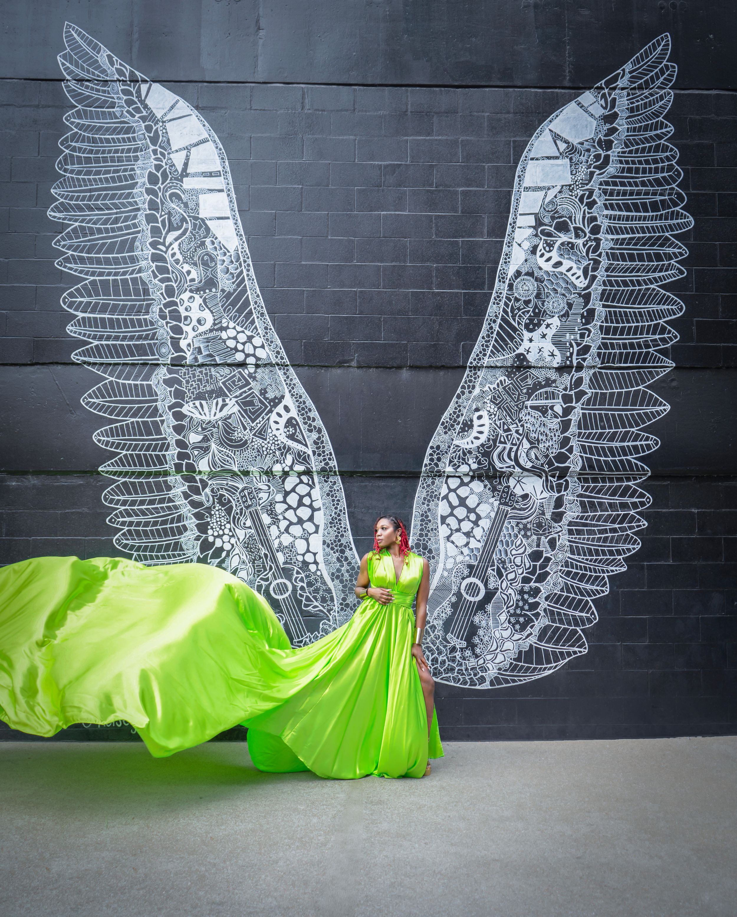 A series showing illuminated white angel wings artwork mounted on a dark wall with a neon green fabric element below.