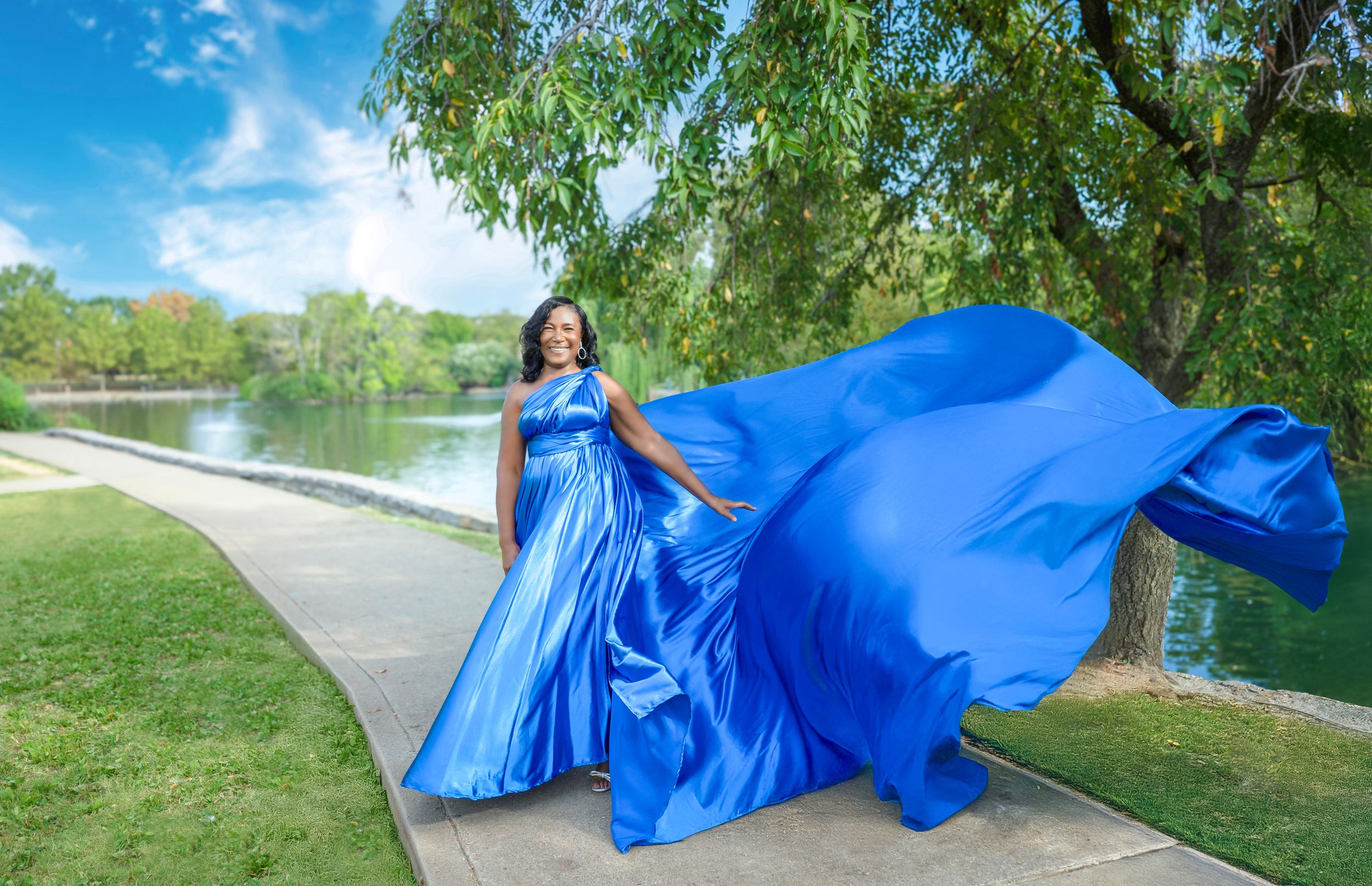 A person in a flowing blue dress twirls gracefully in a series of dynamic poses along a park pathway.