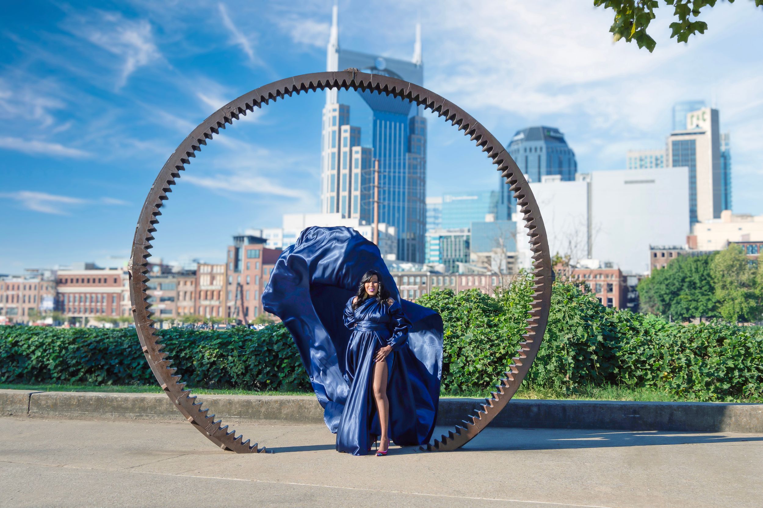 Large metal sculptural arch frames view of Minneapolis skyline and park on sunny summer day.