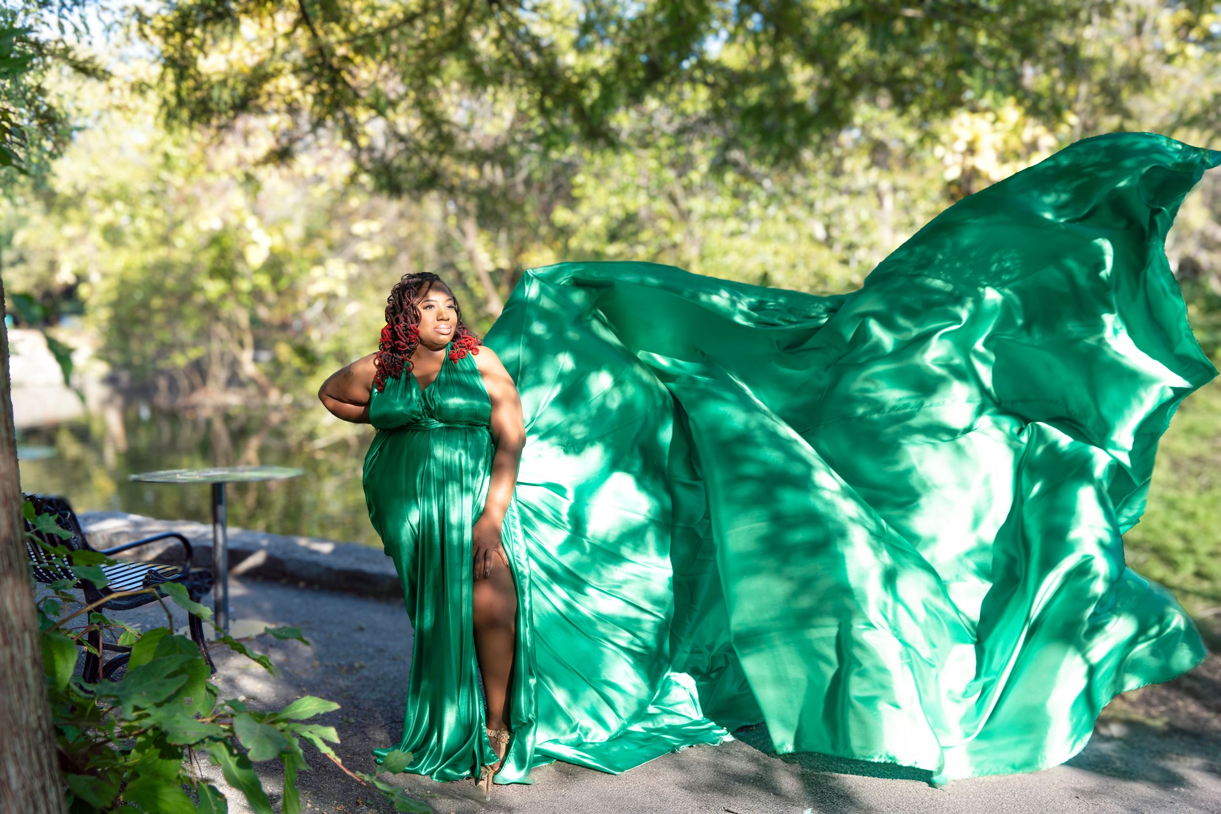 A flowing emerald green dress billows dramatically in the sunlight against a lush outdoor garden setting.