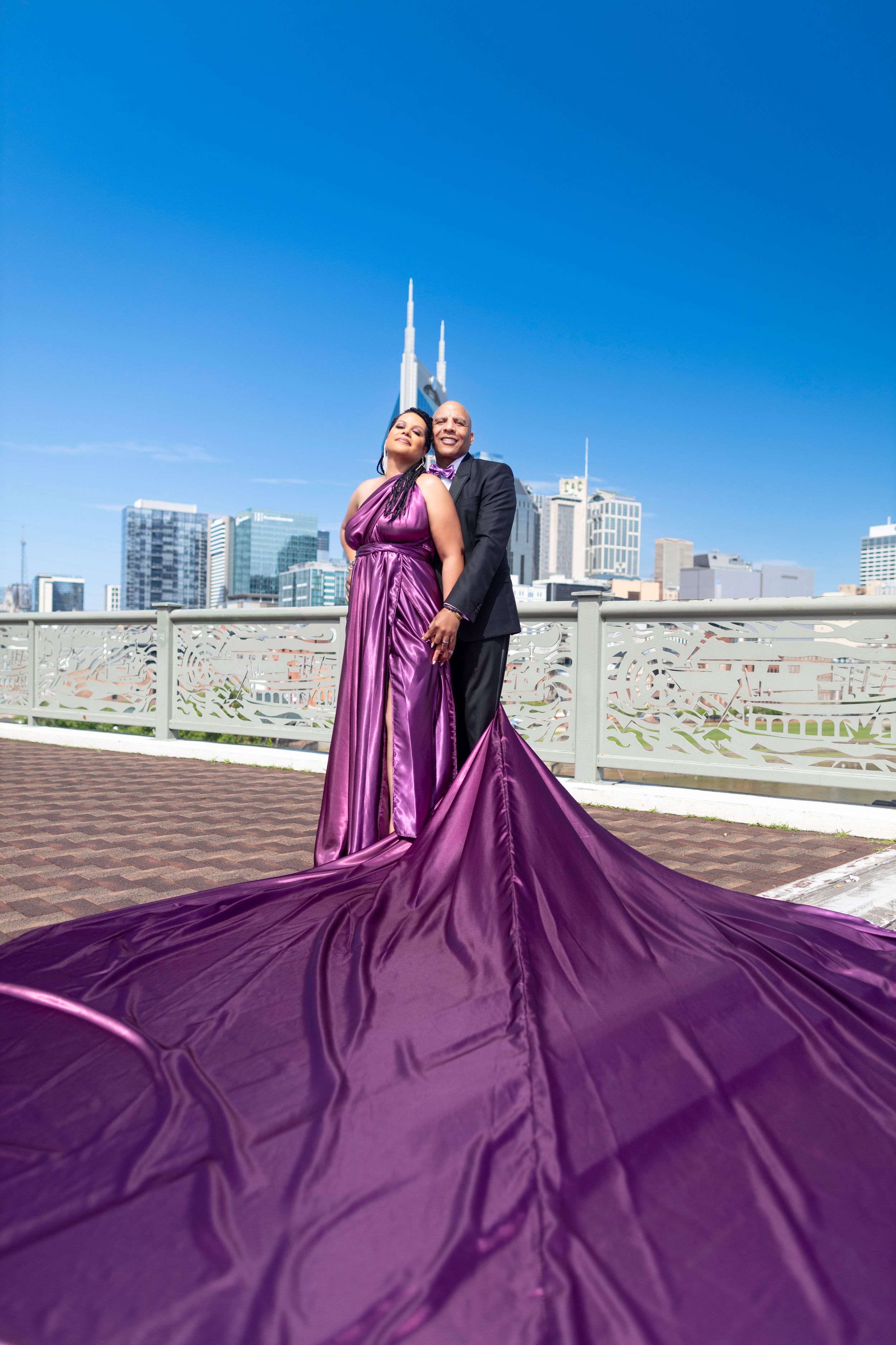 Couple in formal attire with long flowing purple dress pose on rooftop with city skyline and CN Tower in background.