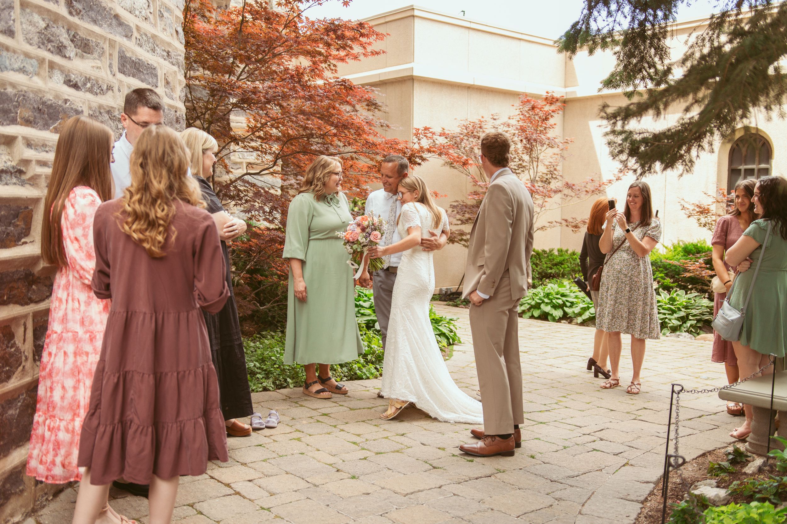 A wedding party poses in an autumn courtyard with pastel colored bridesmaid dresses and falling leaves.