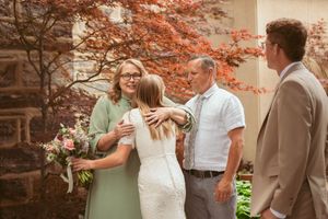 Celebratory moment shared between wedding party members in front of a brick wall with autumn foliage.