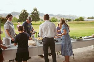 People gather at an outdoor buffet table on a golf course with mountains visible in the background.