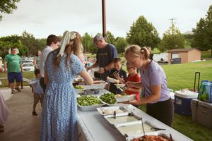 People gather at tables under an outdoor pavilion serving themselves food from a buffet style setup.