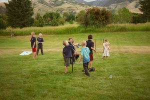People gather at an outdoor park event with mountains visible in the background, enjoying activities on a grassy field.