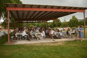 People seated at picnic tables under a large covered patio area during an outdoor event.