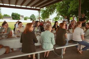 Group of people sitting at long tables under a covered outdoor structure during a gathering.