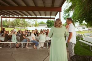 A couple stands before seated guests under a covered outdoor pavilion during a celebration.