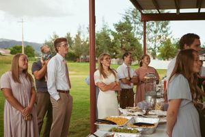 People gather around a buffet table at an outdoor covered venue during what appears to be a casual summer event.