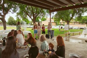 Guests gather at picnic tables under a covered outdoor pavilion for a celebration.