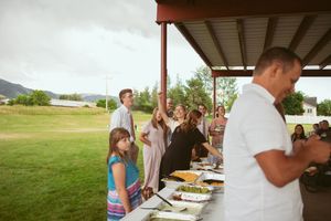 People gathered around a buffet table serving food at an outdoor wedding reception.