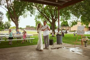 A couple dances under a covered pavilion at an outdoor venue while children play in the background during daytime.