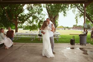 A bride and groom share their first dance together under a rustic park pavilion on a sunny summer day.