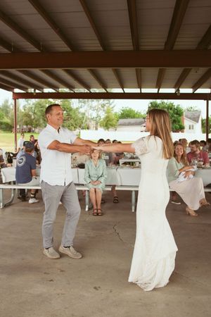 Two people dance together at an outdoor reception while guests watch from picnic tables.