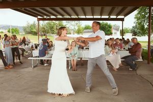 A bride and groom share a romantic first dance under an outdoor pavilion at their rustic wedding reception.