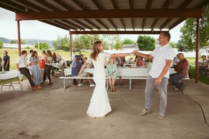 Wedding celebration outdoors under covered pavilion with tables and guests gathered around on a sunny day.