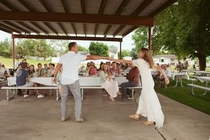 Dancers performing an energetic routine under a covered outdoor venue with spectators seated along edges.