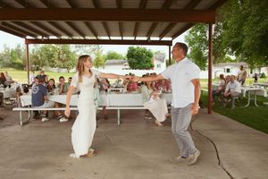 Two people dancing on a concrete floor under a covered outdoor pavilion while others watch from tables.