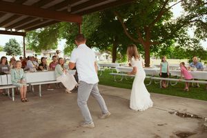 Dancing and celebration taking place under a wooden pavilion at an outdoor wedding reception.
