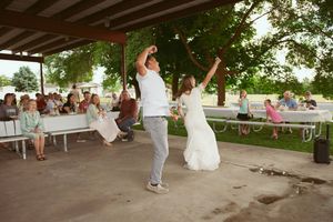 Wedding celebration with joyful dancing at an outdoor covered pavilion with guests seated at tables in the background.