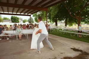 Dancers showing graceful moves on concrete floor beneath wooden shelter as crowd watches from sides.