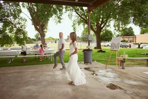 A couple dancing outdoors on a covered patio with trees and lawn visible in the background.