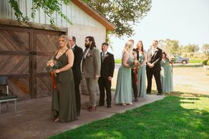 Wedding party in mint and dark green dresses lined up against rustic barn wall outdoors.