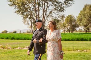 Military service member and guest walk across sunny outdoor venue grounds.