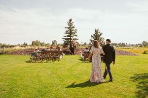 Beautiful outdoor wedding ceremony setup in a rustic field with wooden chairs and decorative floral arrangements.