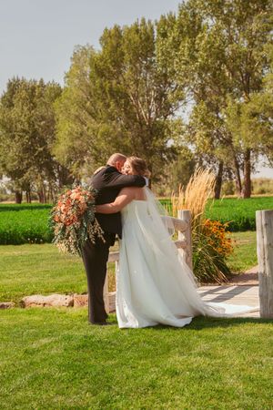 Couple embraces on white bridge surrounded by autumn flowers and greenery.