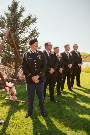 Groomsmen line up outdoors with military service member in dress uniform.