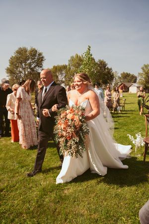 Bride and groom share a romantic kiss on a grassy hillside during their outdoor wedding ceremony.