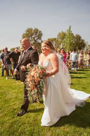 A joyful wedding ceremony processional on a sunny lawn with pink floral bouquet and flowing white gown.