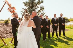 Wedding ceremony under wooden arch decorated with peach flowers.