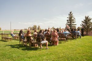 Guests seated in wooden chairs for an outdoor wedding ceremony under blue skies and pine trees.