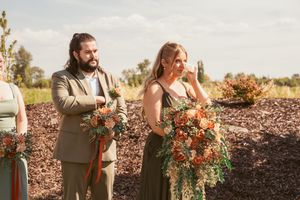 Wedding party members dressed in brown suits and coral dresses pose outdoors during sunset.