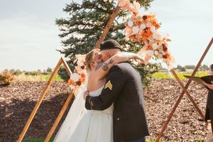 Couple shares intimate moment under wooden arch with peach floral decorations.