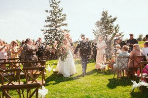 Wedding ceremony guests throw white flower petals into the air during a joyful outdoor celebration moment.