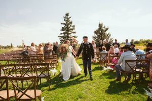 Rustic outdoor wedding ceremony setup with wooden benches and evergreen trees in the background.