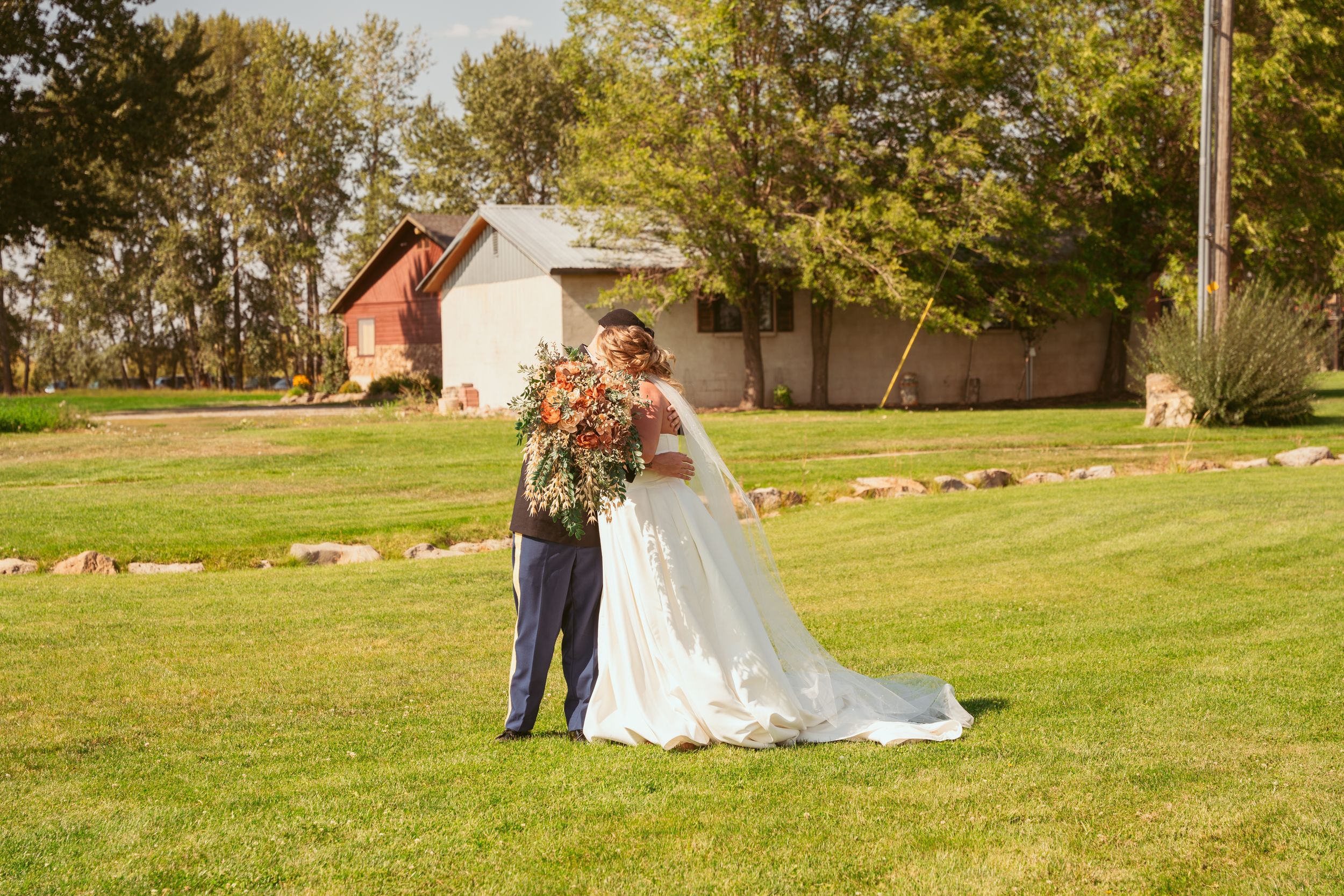 A couple in formal wedding attire share a romantic moment together on a scenic grassy hillside at an outdoor venue.