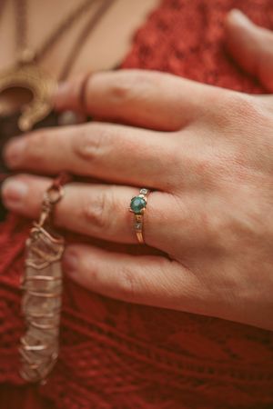 Delicate turquoise stone ring worn on hand against red knit fabric background.
