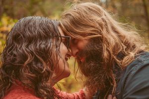 A loving couple with long wavy hair share an intimate moment together outdoors during autumn.