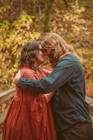 A warm embrace is shared between two figures in autumn, one wearing a deep red dress and the other in navy blue.