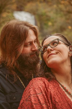 A romantic outdoor portrait of a couple with long-haired bearded partner and partner in glasses sharing an intimate moment.