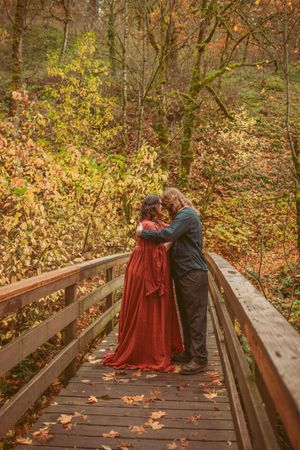 A couple shares an intimate moment on a wooden boardwalk surrounded by autumn foliage in the forest.