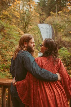 Two people in autumn attire sitting close together on a bench surrounded by fall foliage.