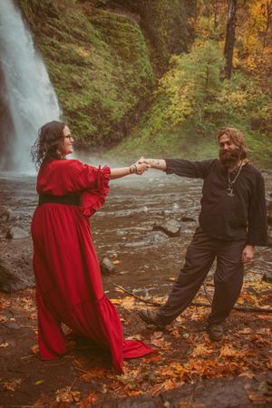 A playful dance pose near a cascading waterfall surrounded by autumn leaves and natural scenery.