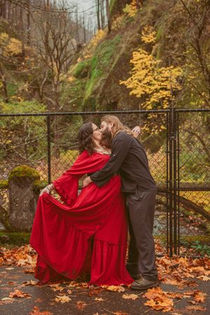 Romantic dance poses captured along a fence with autumn leaves scattered on the ground.
