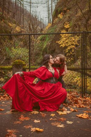 A dramatic autumn portrait with a twirling red dress against a rustic bridge and fall foliage background.